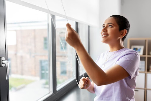 A woman closing the blinds on a window.