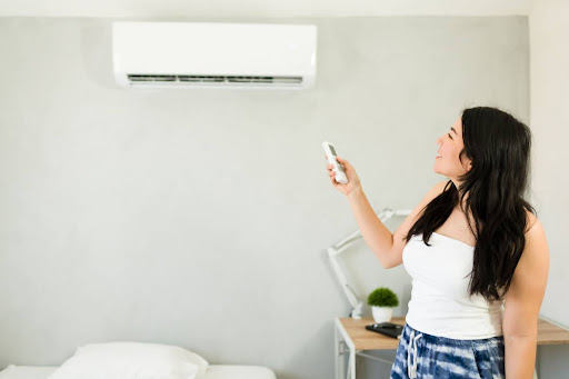 A woman pointing a remote control at an indoor mini-split unit on a wall.