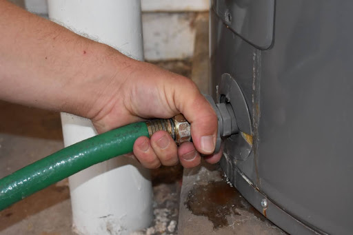 A hand connecting a hose to a water heater drain valve.