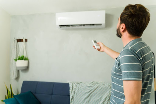 A man pointing a remote at an indoor ductless mini-split unit on a wall.