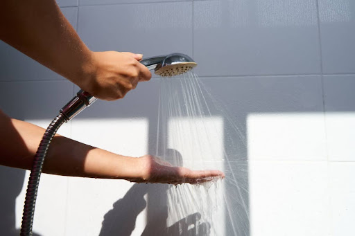 A hand touching the water pouring from a shower head, checking water temperature.