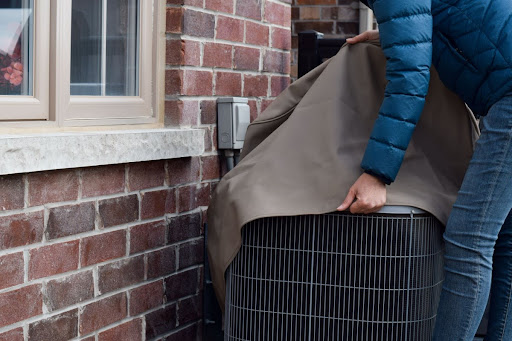 A man in a winter coat putting a cover on an outdoor AC unit.