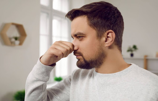 A man holding his nose due to a bad smell in a home.