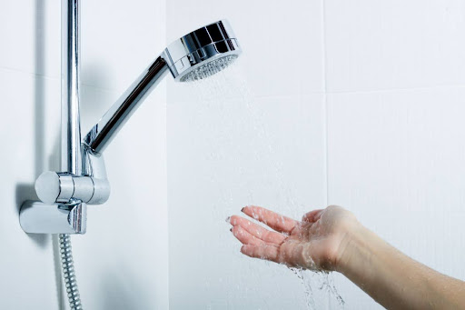 A hand feeling the water flowing for a shower head.